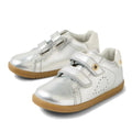 The Bobux IW Iwalk Maverick Leather Sneaker Silver features shiny silver leather, light brown soles, double velcro straps, side perforations for breathability, and metallic details—perfect for kids.