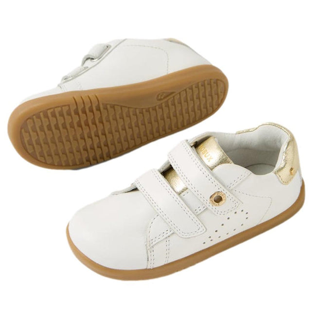 The Bobux IW Iwalk Maverick Leather Sneaker in White Gold features kids’ leather uppers, light brown rubber soles, gold accents on the heel and tongue, and two adjustable straps. One toddler sneaker stands upright; the other displays its sole., 9420074836533, 9420074836540, 9420074836557, 9420074836564