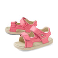 The Bobux IWalk Strand Sandal in Pink Lemonade is an open-toe leather sandal for toddlers, featuring adjustable velcro straps and beige soles. Shown at a slight angle on a white background, these stylish and comfortable sandals are perfect for little feet.