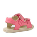 The Bobux IWalk Strand Sandal in Pink Lemonade for toddlers features a soft leather upper, a beige sole, open heel, and adjustable Velcro straps, as seen from an angled view highlighting the back and side.