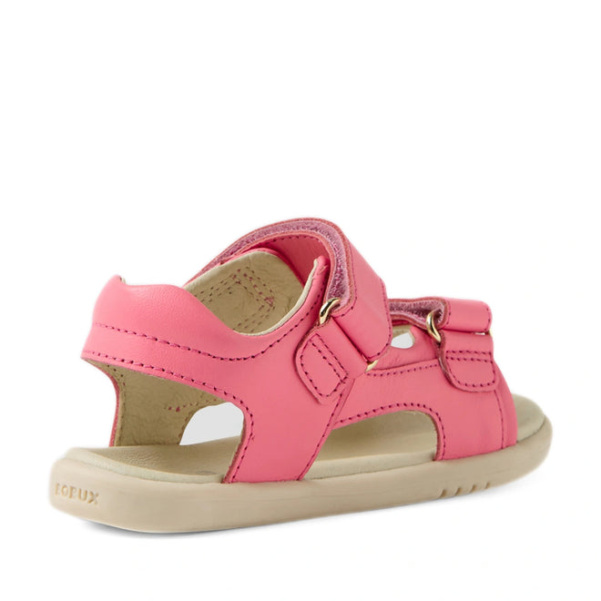 The Bobux IWalk Strand Sandal in Pink Lemonade for toddlers features a soft leather upper, a beige sole, open heel, and adjustable Velcro straps, as seen from an angled view highlighting the back and side.