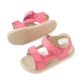 A pair of Bobux IWalk Strand Sandal Pink Lemonade Open Toe Toddlers, featuring soft pink leather, adjustable Velcro straps, and beige soles, is displayed from the side and bottom against a white background. These washable sandals are crafted for comfort and convenience.