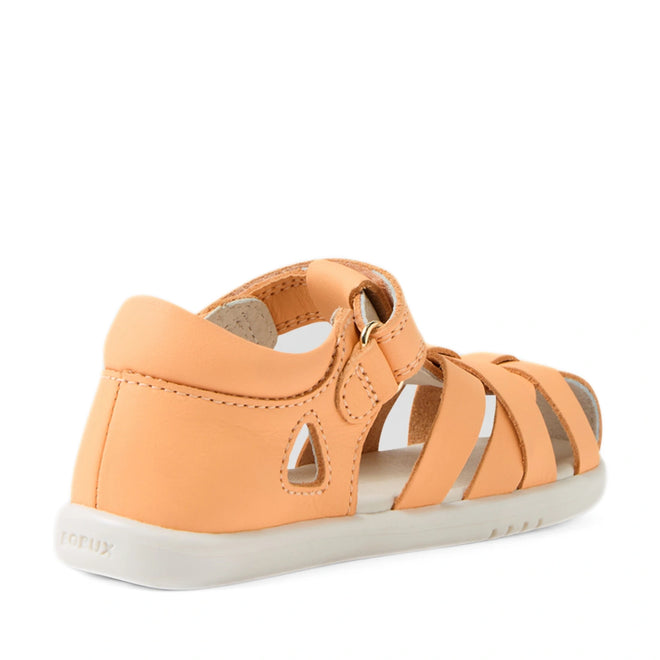 A peach-colored Bobux Iwalk IW Tropicana II Jelly Leather Sandal, viewed from the back right side, features a closed heel, white sole, and adjustable strap. This toddler sandal offers cutout details, stitched seams for added style and comfort, and provides closed-toe protection ideal for little ones., 9420074810083, 9420074810090, 9420074810106, 9420074810113, 9420074810120