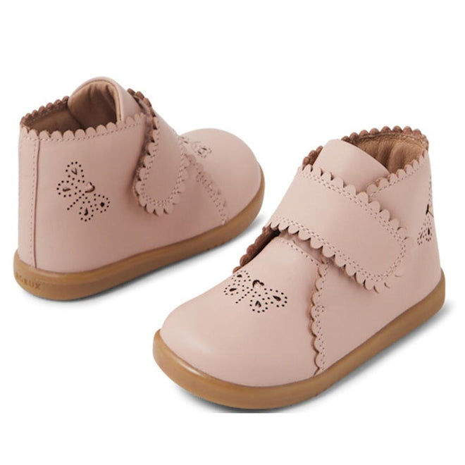 The Bobux IW Iwalk Willow Leather Boot in Cameo Rose Pink features scalloped edges, butterfly cutout designs, tan soles, and adjustable hook-and-loop straps for toddlers.