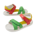 The Bobux KP Kids Plus Dune Leather Sandal in Grenadine Red features green and red adjustable straps, a yellow lining, and white soles, offering both comfort and style for little feet. The sandals are displayed against a white background.