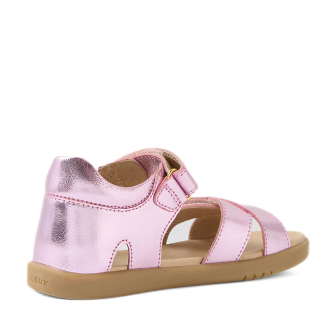 Introducing the Bobux KP Kids Plus Flora Leather Sandal in Pink Lemonade: these children’s sandals feature a metallic pink finish with an open-toe design, adjustable Velcro strap, and a durable brown rubber sole, displayed from both the back and side views.