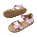 Two metallic pink Bobux KP Kids Plus Flora Leather Sandal Pink Lemonade kids sandals with tan soles are shown. One sandal is positioned upright, while the other displays the textured bottom. These adjustable leather sandals feature open toes and velcro straps across the toes and around the ankle.