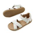 The Bobux KP Kids Plus Flora Leather Sandal in White Floral is an adjustable kids sandal featuring tan soles and white straps adorned with a pastel nature print of leaves and flowers. One sandal is displayed from the side, while the other is shown from the bottom.