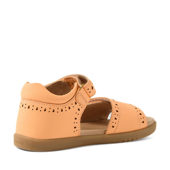 Bobux Kid+ Plus KP Logan Peach Jelly Open Toe Sandal for kids, featuring a peach-colored design with cutout details, closed heel, open toe, adjustable velcro strap, and a flat tan rubber sole, displayed at an angle on a white background.