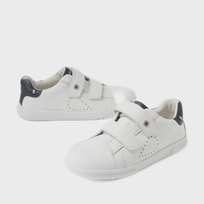 A pair of Bobux Kid+ Plus KP Maverick Leather Sneakers in White Navy—children’s sneakers with adjustable velcro straps, dark blue heel accents, and crafted from breathable leather for comfort—are stylishly displayed on a white background.
