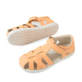 A pair of Bobux Kids Plus KP Tropicana II Peach Jelly Quick Dry Sandals, featuring a peach hue, closed-toe leather design with crisscross straps, white soles, and a hook-and-loop ankle strap. One sandal is pictured in profile while the other displays the sole. These podiatrist-approved kids’ shoes are crafted for both comfort and style., 9420074861368, 9420074861337, 9420074861344, 9420074861351, 9420074861375