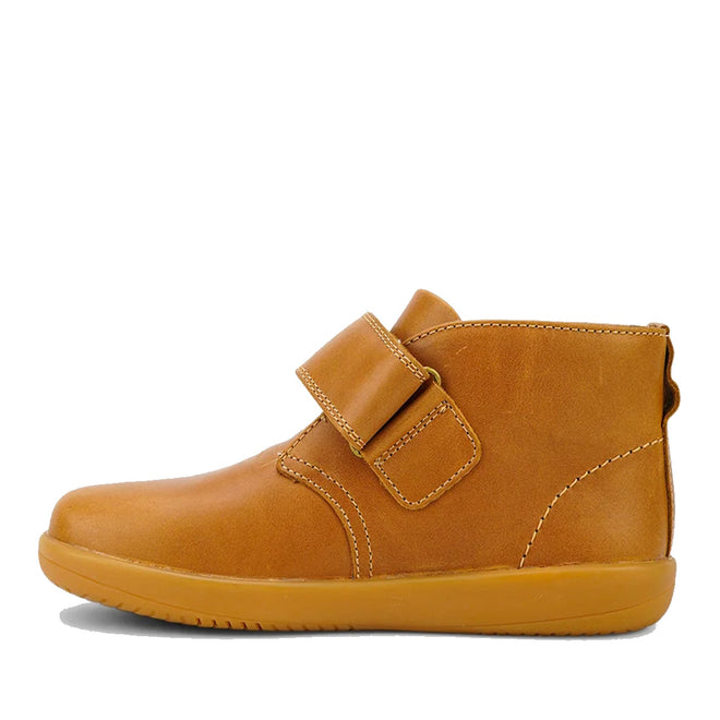 The Bobux Kid+ Desert Boot Caramel 830305Z inner foot view is a brown leather unisex children’s high-top boot with a tan rubber sole and wide hook-and-loop strap, shown in side profile against a white background., 9420068516861, 9420075719682, 9420075719699, 9420068516892, 9420068516908, 9420068516915, 9420068516922