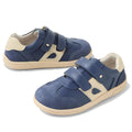 The Bobux KP Kids Plus Titan Juniors Leather Sneaker in Vintage Indigo Blue features leather uppers, beige accents, Velcro straps, perforated details, and a sturdy rubber sole. One shoe stands upright; the other lies on its side.