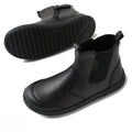 The Bobux Kid+ Black School Leather Boot Jodhpur II features black leather, ankle-high design, pull tabs, side elastic panels, and textured black rubber soles. One boot is upright; the other displays the sole’s pattern.