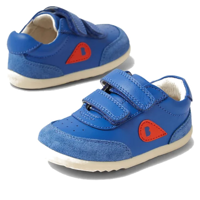 The Bobux Step Up SU Champ II Sneaker Olympian Blue features velcro straps, white soles, suede toe caps, and a red side patch with a small blue heart—perfect first walker shoes.