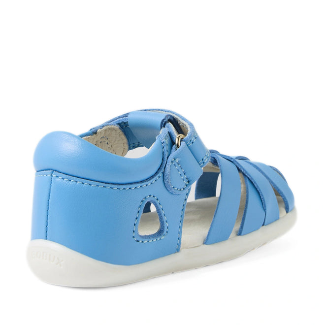 The Bobux Step Up SU Tropicana II Baltic Sea Blue Closed Toe Sandal is shown from a rear side angle. This toddler leather sandal features a closed heel, open sides, white sole, and a convenient hook-and-loop strap inspired by Bobux Tropicana sandals for easy fastening., 9420074809957, 9420074809964, 9420074809971