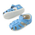 Two Baltic Sea Blue toddler leather Bobux Step Up SU Tropicana II Closed Toe Sandals with white soles. One sandal is positioned upright, revealing the top and side view, while the other is flipped to showcase the sole. The sandals have a woven design and a hook-and-loop strap, embodying classic closed-toe sandal style for extra protection and comfort., 9420074809957, 9420074809964, 9420074809971