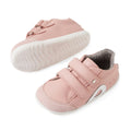 A pair of Bobux SU Step Up Blaze Leather Toddlers Sneaker in Ballet Pink, featuring white soles, Velcro straps, and a gray inner lining—perfect first walking shoes for your little one. One sneaker is upright while the other lies on its side to showcase the sole., 9420074848901