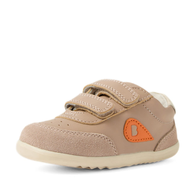 The Bobux Step Up SU Champ Sneaker First Walker in Warm Taupe is a light brown toddler shoe featuring two hook and loop straps, an orange patch detail, and a beige sole, shown on a white background—perfect first walkers crafted in kids’ leather sneakers style., 9420074861894, 9420074861900, 9420074861917