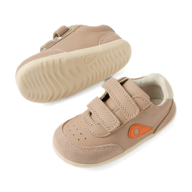 A pair of Bobux Step Up SU Champ Sneaker First Walker shoes in Warm Taupe, featuring light brown uppers with hook and loop straps, beige soles, suede toe caps, and an orange side detail. One shoe is upright while the other displays the sole., 9420074861894, 9420074861900, 9420074861917
