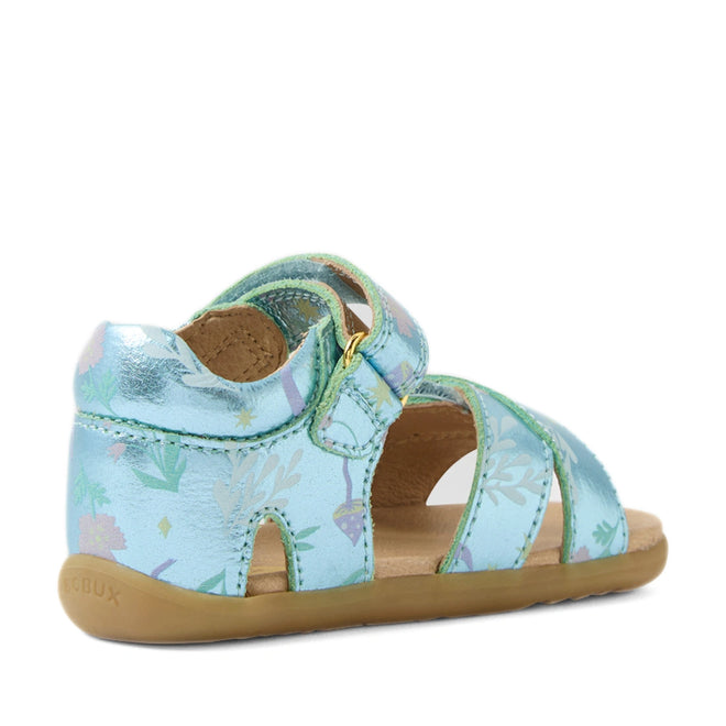 Bobux Step Up Flora First Walker Jelly Mint Metallic Blue sandal for toddlers, featuring shiny metallic blue leather with pastel floral patterns, an ankle strap with hook-and-loop closure, open sides, and a soft brown sole. The sandal is angled to show the back and side.
