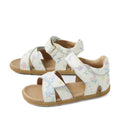 The Bobux Step Up Flora First Walker Sandal in White Floral is a pair of children’s open-toe, open-heel leather sandals featuring pastel-colored floral and plant patterns on a white background, beige soles, and adjustable straps—perfect as little ones’ first walking sandals.