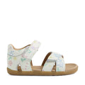 The Bobux Step Up Flora First Walker Sandal White Floral is a children’s sandal crafted from white leather with pastel floral patterns. Designed for early steps, it features hook-and-loop ankle and toe straps for a secure fit, an open toe, and a tan sole. The sandals are displayed in profile against a plain white background.