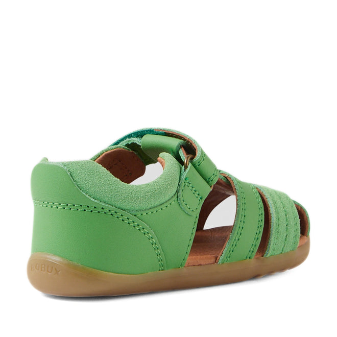 A rear side view of the Bobux Step Up Sandal Roam Closed Toe Sandals in Retro Green for children, featuring green leather with a closed toe and heel, open sides, an adjustable strap, brown sole, and visible stitching—ideal as first walker shoes., 9420074807205, 9420074807212, 9420074807229