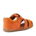The Bobux Step Up Sandal Roam Closed Toe Sandals in Orange Peel are toddler sandals inspired by the classic Bobux Roam design, featuring a closed heel, open toe, and adjustable strap. Shown from a rear side angle, these sandals combine a light brown, slightly textured sole with the comfort of toddler leather sandals and the stylish look of closed-toe footwear., 9420074807250, 9420074807267, 9420074807274