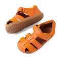 The Bobux Step Up Sandal Roam Closed Toe Sandals in Orange Peel are displayed on a white background. One sandal stands upright while the other is tilted to reveal the tread pattern, showcasing the quality and design of these toddler leather sandals with Velcro straps and rubber soles.