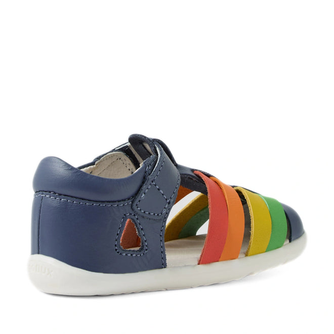 The Bobux Step Up SU Toddlers Tidal Vintage Indigo Blue Closed Toe Sandal is a stylish and water-friendly leather sandal for children, featuring a vintage indigo blue heel and multicolored straps in orange, red, yellow, and green. Designed with a durable white sole and a small cutout on the side, these closed-toe sandals combine vibrant design with practical comfort for little feet., 9420074808578, 9420074808585, 9420074808592, 9420074808608