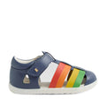 A navy blue Bobux Step Up SU Toddlers Tidal Vintage Indigo Blue Closed Toe Sandal with a white sole and rainbow-colored straps (red, orange, yellow, green) across the top. This water-friendly leather sandal, inspired by the Bobux Tidal First Walking Sandals, features a Velcro ankle strap, a small gold heart detail, and a closed-toe design ideal for little adventurers., 9420074808578, 9420074808585, 9420074808592, 9420074808608