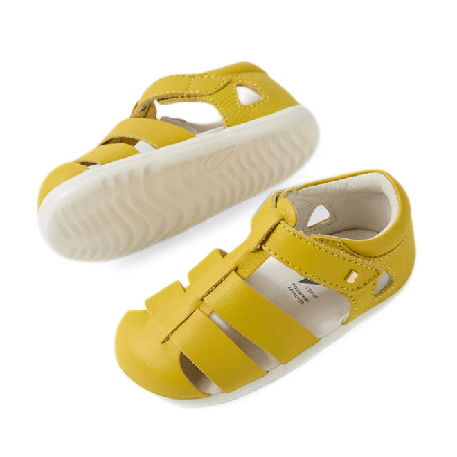 A pair of Bobux Step Up SU Toddlers Tidal Mango Mint Yellow Closed Toe Sandals featuring white soles, open toes, and a closed heel. Made from water-friendly leather, one sandal stands upright while the other rests on its side to showcase the textured sole—ideal as first walker sandals for adventurous little explorers., 9420074808639, 9420074808646, 9420074808707