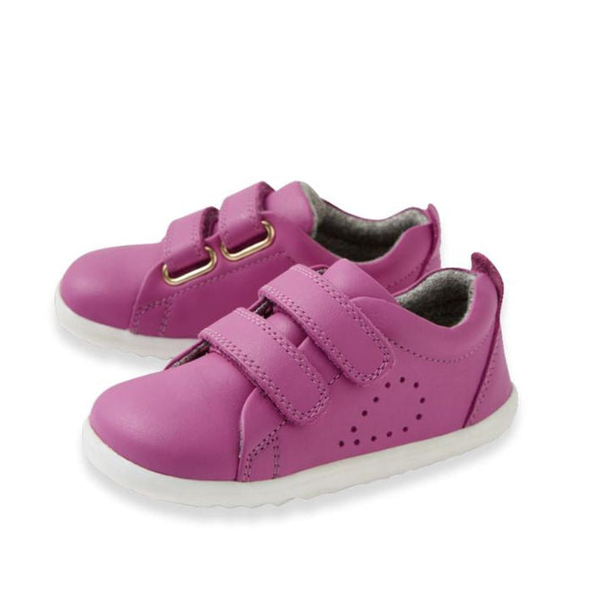 A pair of Bobux Step Up Grass Court Trainer Cattleya Orchid Purple Shoes with white soles, two velcro straps per shoe, and small side perforations—ideal stylish first walkers for toddlers.