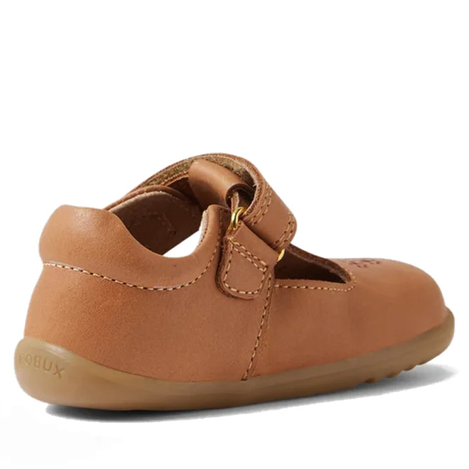 The Bobux Step Up T-Bar Rosie First Walker Shoe in Caramel Tan is a toddler leather flat with a hook-and-loop strap, flexible rubber sole, and BOBUX embossed on the heel—perfect for first walkers, shown from the back-left angle., 51165, 9420074850041, 9420074850058, 9420074850065