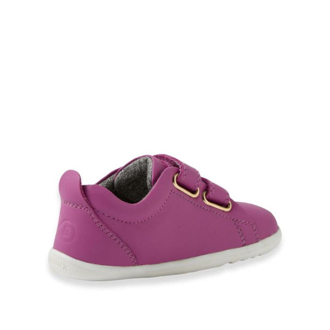 A small, bright purple Bobux Step Up Grass Court Trainer Cattleya Orchid shoe for toddlers with two velcro straps, gold eyelets, white sole, and gray lining shown from a rear side angle—perfect stylish first walker shoes., 9420074806499, 9420074806505, 9420074806512, 9420074806529