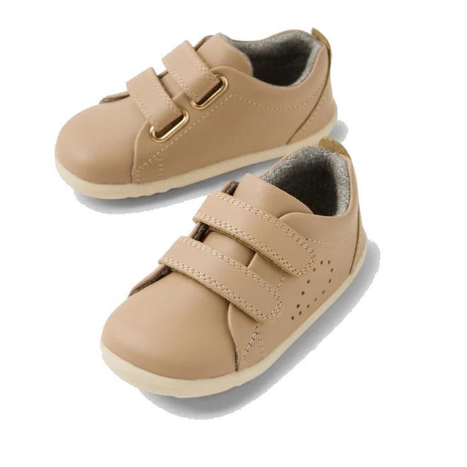 Bobux Step Up Grass Court Trainer Warm Taupe Shoes: beige leather toddler sneakers with white soles and two hook-and-loop straps, shown from two angles on a white background—ideal first walker street-style shoes.