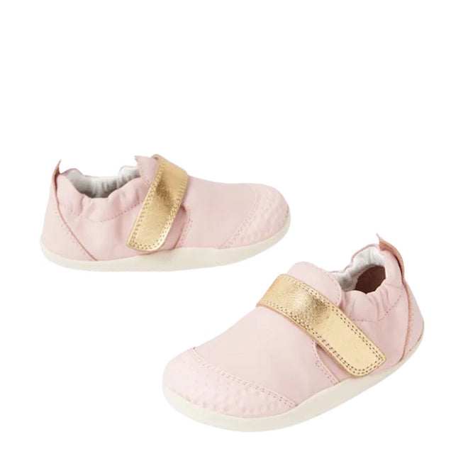The Bobux XP Xplorer First Walking Shoes Go Ballet Pink are soft pre-walker leather shoes with white soles and shiny gold Velcro straps, featuring a flexible sole for baby's first steps, shown on a white background.