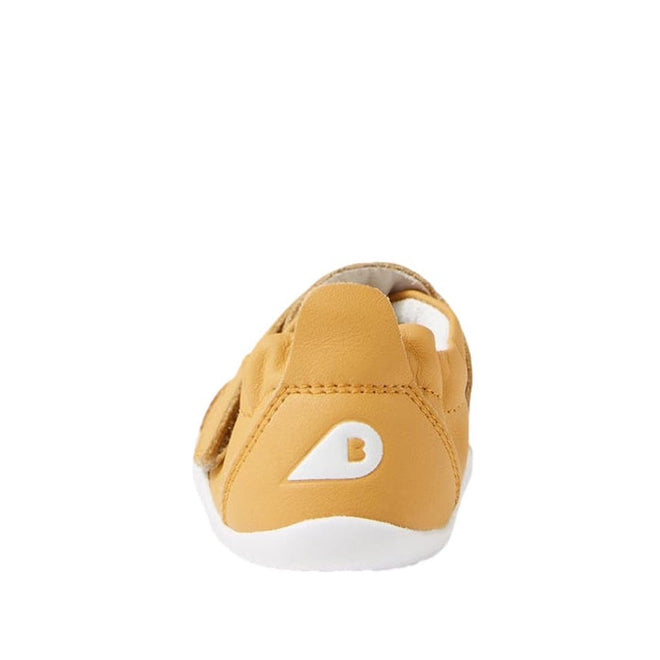The Bobux XP Xplorer First Walking Shoes Go Oak Buff Tan are tan pre-walker leather shoes seen from the back, with a flexible white sole and a white triangle B logo on the heel, set against a plain white background., 9420068567962, 9420068567979, 9420068567986