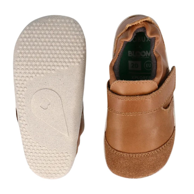 The Bobux Explorer Marvel Caramel Dress Shoe First Walker is shown from the top and bottom, featuring brown leather, a soft flexible sole with grip, hook-and-loop strap, scuff-resistant design, and light soles with a teardrop logo.