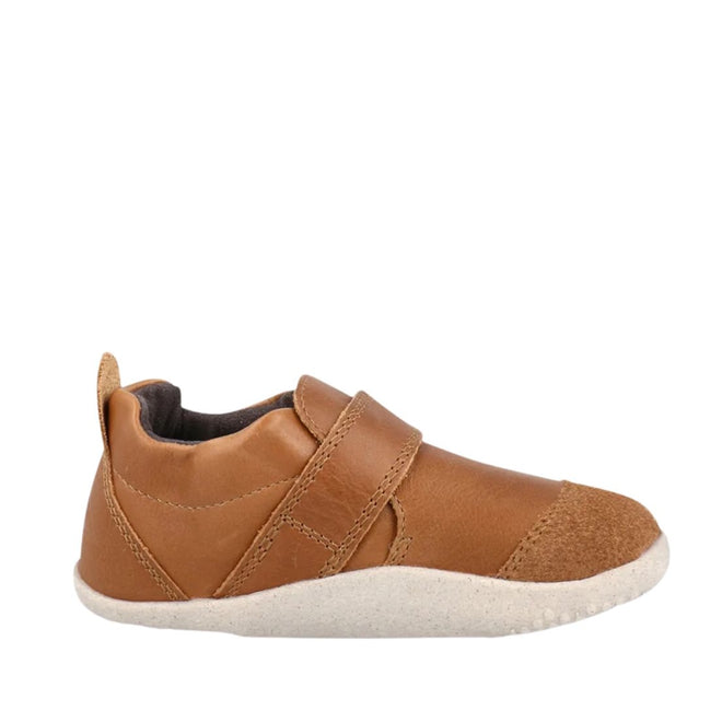 Bobux Explorer Marvel Caramel Dress Shoe First Walker: a brown leather baby shoe with a white rubber sole, hook-and-loop strap, and suede toe cap. These scuff-resistant toddler shoes are shown in side profile on a white background.