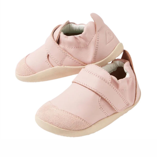 The Bobux Explorer Marvel Ballet Pink Dress Shoe First Walker is a light pink leather baby shoe with Velcro straps, soft soles, rounded toes, suede toe accents, a smooth finish, and a small logo on the side.