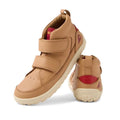 The Bobux Kid+ Trek Leather Boot Sandstorm 853802 is a pair of tan leather children's sneakers featuring velcro straps, a barefoot-shaped toe-box, white textured soles, and red heel accents, shown from front-side and rear angles.