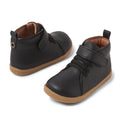 The Bobux Iwalk Voyager Toddlers Leather Boot Black 650603 features black leather, brown flexible soles, hook and loop straps, and decorative laces. This unisex toddler boot is shown on a white background.