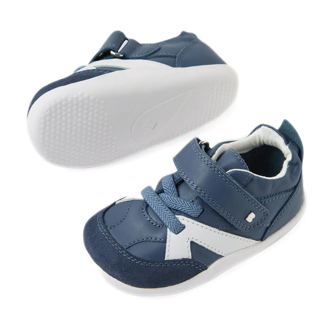 A pair of Bobux Xplorer XP Chase Vintage Indigo Blue First Walker Crawlers, featuring blue and white design with white rubber soles—one shoe upright and the other displaying its textured sole—complete with laces and a hook-and-loop strap, perfect for your little one’s pre-walking or first steps., 9420074850638, 9420074850645, 9420074850652, 9420074850669