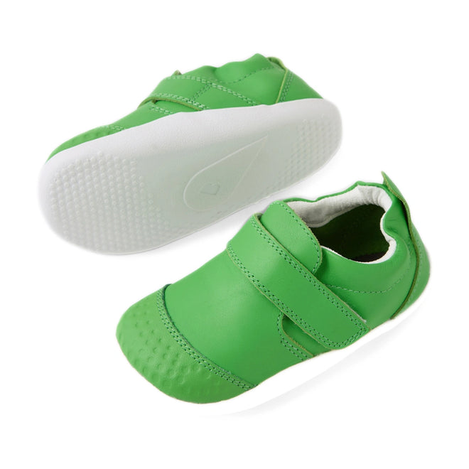 A pair of Bobux Xplorer XP Go Retro Green First Walker Crawler baby shoes, featuring a small, bright green design with white soles and Velcro straps. One shoe stands upright while the other lies on its side to display the textured sole—perfect for little ones taking their first steps., 9420074808981, 9420074808998, 9420074809001
