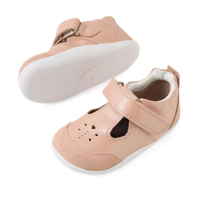 Introducing the Bobux XP Explorer Rue First Walker Sandal Camo Rose Pink—a pair of light pink leather T-bar shoes featuring white flexible soles, Velcro straps, and charming heart-shaped cutouts on the toe area. One sandal stands upright while the other is angled to display its flexible sole—making these sandals perfect for your little one’s first steps., 9420074851246, 9420074851253, 9420074851260