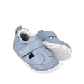 The Bobux XP Explorer Beau First Walker Sandal 502303 features light blue uppers, white flexible soles, Velcro straps, and front cutout details, displayed against a white background.