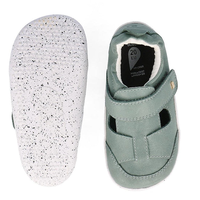 The Bobux XP Explorer Beau First Walker Sandal in Sage Green features white, speckled rubber soles, a hook-and-loop strap, and a flexible sole with a dotted tread pattern. One shoe is shown top-down; the other displays the sole., 9420075784499, 9420075783676, 9420075783706, 9420075784208