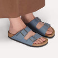 A person stands on a light surface wearing a brown skirt and BIRKENSTOCK Arizona Birko Flor Balsat Grey Regular Width 2 Strap Sandals with supportive cork-latex footbeds., 51737, 51738, 51739, 4067707675807, 4067707675845, 4067707675883, 4067707675920, 4067707675968, 4067707676002, 4067707676040, 51747, 51748, 51749